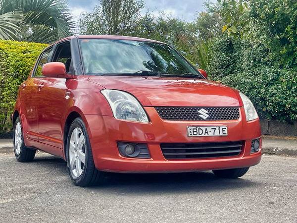 Used Suzuki For Sale - Photo showing Suzuki Swift in Sunset Orange colour from the driver drivers side angle view