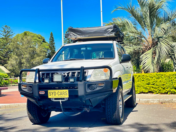 Used Toyota Prado for Sale - Manual 2008 Turbo Diesel Model with heavy duty Roo bars and roof rack + Roof Top Tent - photo showing the front passenger side angle view with roobars and the roof top tent folded away ready for an adventure around Australia