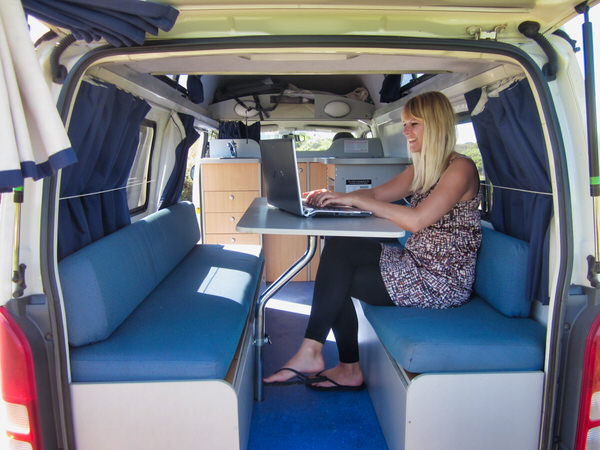 Toyota Hiace Campervan for Sale - Ready to travel around Australia - Photo showing Sara sitting in the lounge area of the campervan using her laptop