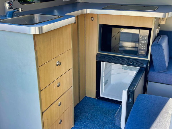 Toyota Hiace Campervan for Sale - Ready to travel around Australia - Photo showing the view of the L shaped kitchen with twin gas burner, microwave, 55L fridge, workstop space and easy to use practical kitchen area